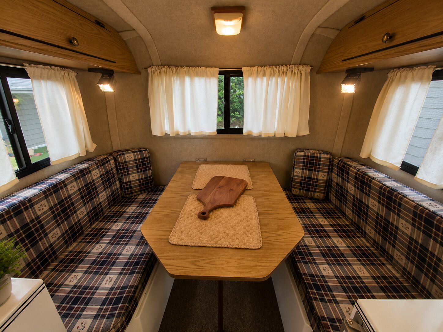 A cozy RV interior with a central table, plaid-patterned seating, and curtains.
