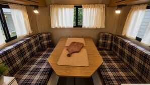 Un intérieur de camping-car chaleureux, avec une table centrale, des sièges à motifs écossais et des rideaux.