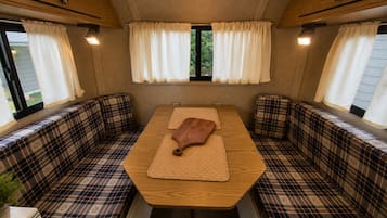 A cozy RV interior with a central table, plaid-patterned seating, and curtains.