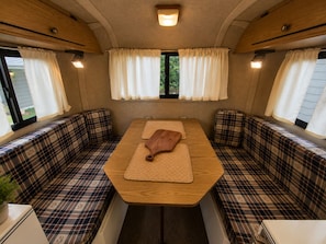 A cozy RV interior with a central table, plaid-patterned seating, and curtains.