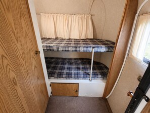 A compact bunk bed with a checkered mattress pattern, a small wooden door, and a window with curtains.