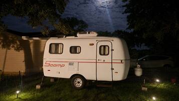 A Scamp RV parked in a grassy area at night with a full moon in the background.