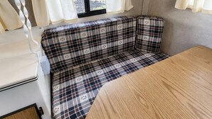 Un intérieur de camping-car compact, avec une banquette à carreaux, une petite table et une fenêtre avec des rideaux.