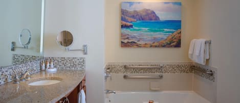 A bathroom with a double sink, a bathtub, a handrail, and a painting of a coastal scene.