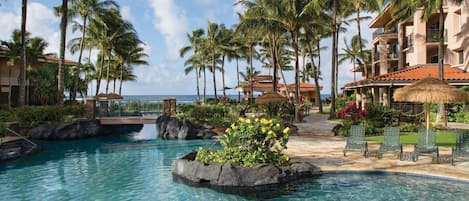 A resort pool with clear water, surrounded by palm trees and a building with a red-tiled roof.