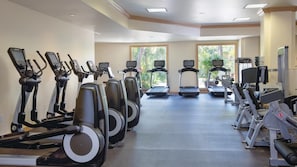 Un gimnasio con diversas máquinas de cardio, una cinta de correr y equipo de pesas.