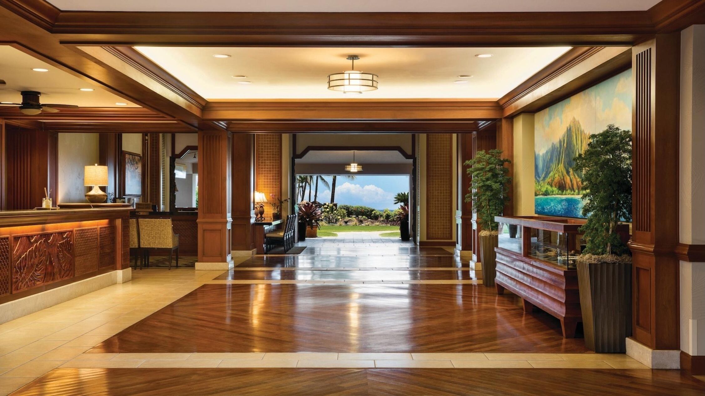 A spacious lobby with a wooden floor, a reception desk, a seating area, and a large painting of a mountain landscape.