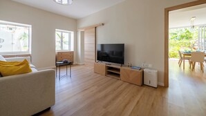 A modern living room with a flat-screen TV, wooden flooring, and a sliding door leading to a balcony with plants. - Dreamscape Levada (Funchal)