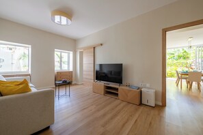 Ein modernes Wohnzimmer mit Flachbildfernseher, Holzboden und einer Schiebetür zu einem Balkon mit Pflanzen.