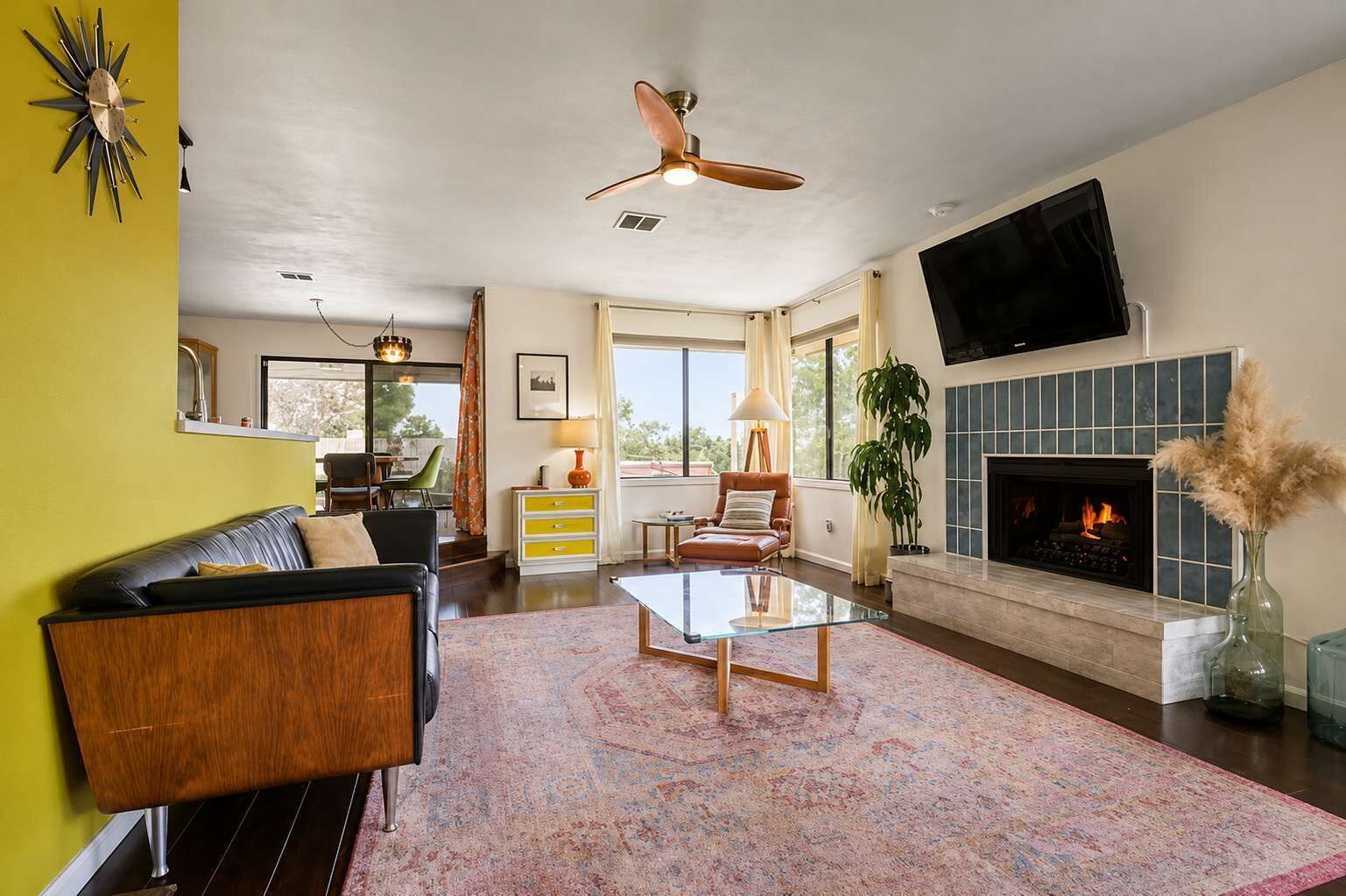 A living room with a fireplace, a ceiling fan, and a television mounted on the wall.