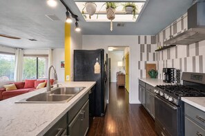 A modern kitchen with a central island, stainless steel appliances, and a view to the living area. - Chromocamino · Pool, Hot Tub, Mini Putt, Game Room (Yucca Valley)