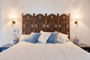 Een bed met een houten hoofdeinde, twee nachtkastjes en twee wandlampen.