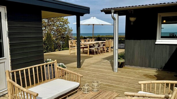 A wooden deck with outdoor furniture, including a table and chairs, and a view of the ocean. - Renovated seaside home with ocean view (Frederikshavn)