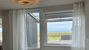 A room with a bed, a window with curtains, a ceiling light fixture, and a view of the outdoors. - Renovated seaside home with ocean view (Frederikshavn)