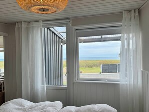 A room with a bed, a window with curtains, a ceiling light fixture, and a view of the outdoors. - Renovated seaside home with ocean view (Frederikshavn)
