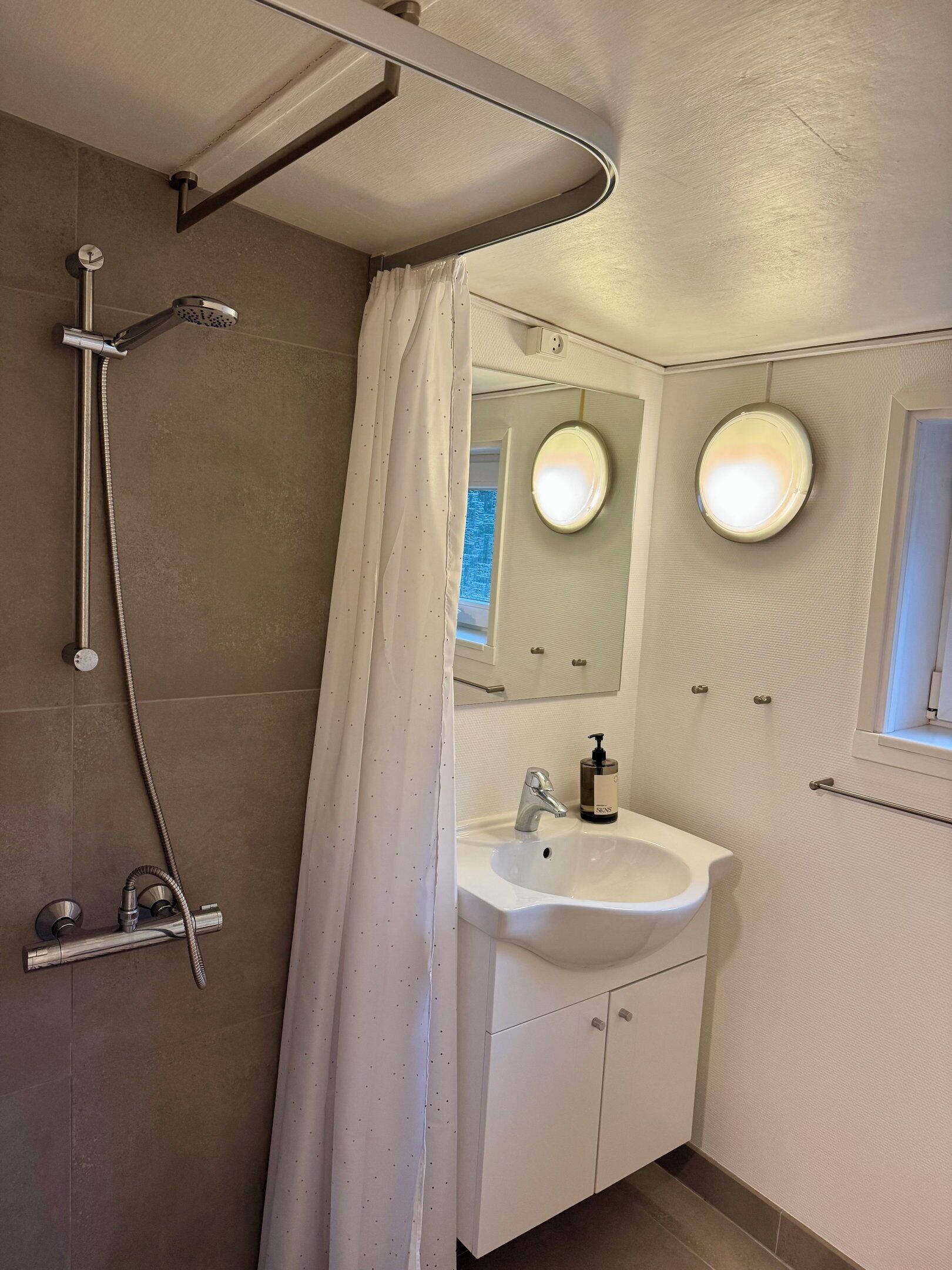 A bathroom with a shower, a sink, and two mirrors.