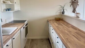 A narrow kitchen with white cabinets, a wooden countertop, and a built-in oven. - Renovated seaside home with ocean view (Frederikshavn)