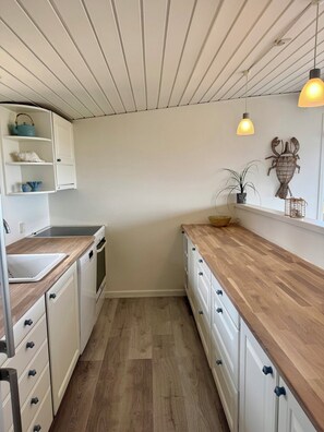 A narrow kitchen with white cabinets, a wooden countertop, and a built-in oven. - Renovated seaside home with ocean view (Frederikshavn)