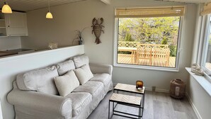 A modern living room with a sofa, a coffee table, and a window with a view of an outdoor deck. - Renovated seaside home with ocean view (Frederikshavn)