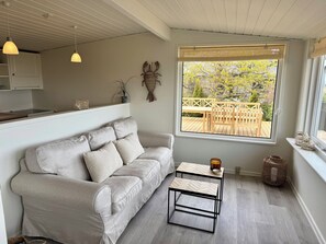 A modern living room with a sofa, a coffee table, and a window with a view of an outdoor deck. - Renovated seaside home with ocean view (Frederikshavn)