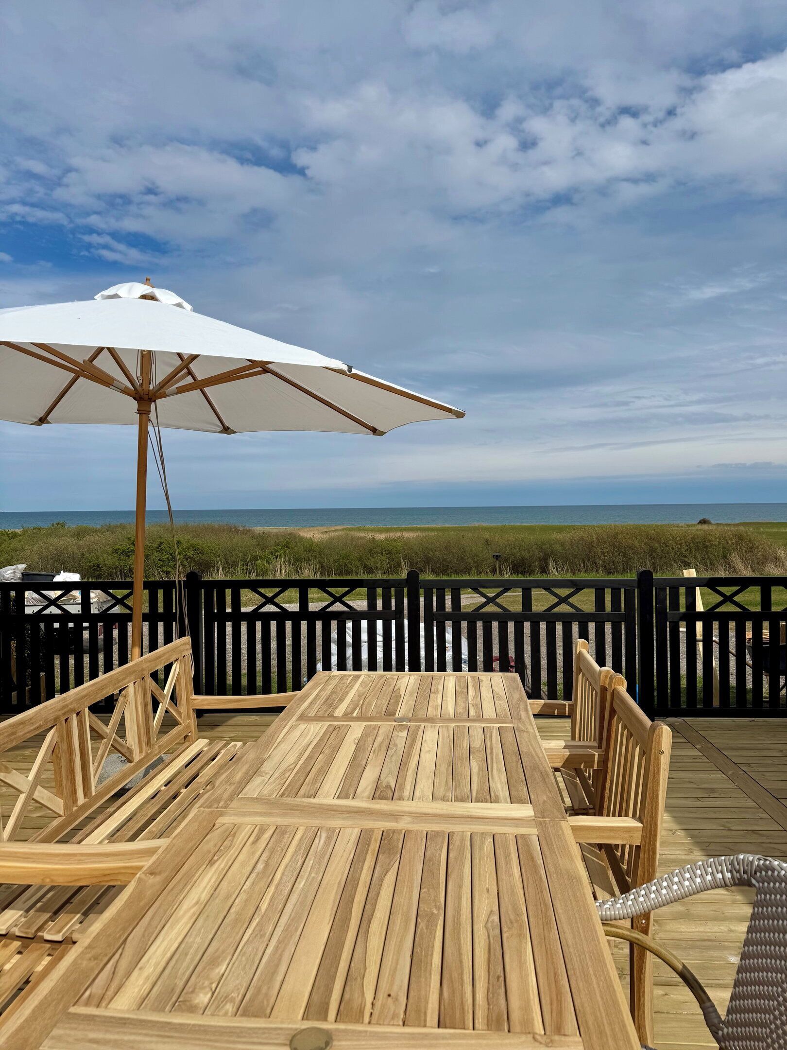 Una terraza de madera con una mesa, sillas y una sombrilla, con vista al océano.