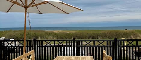 A wooden deck with a table and chairs, an umbrella, and a view of the ocean.