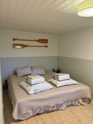 A bedroom with a bed, pillows, a lamp, and two wooden paddles on the wall.