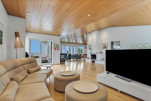 Een ruime woonkamer met een moderne bank, poufs, een flatscreen-tv en een open haard.