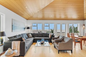 A modern living room with a sectional sofa, a glass coffee table, and a dining area with a wooden table and chairs. - Spacious 340 m² Home with Stunning City & Mountain Views, Gym and Garden (Reykjavík)