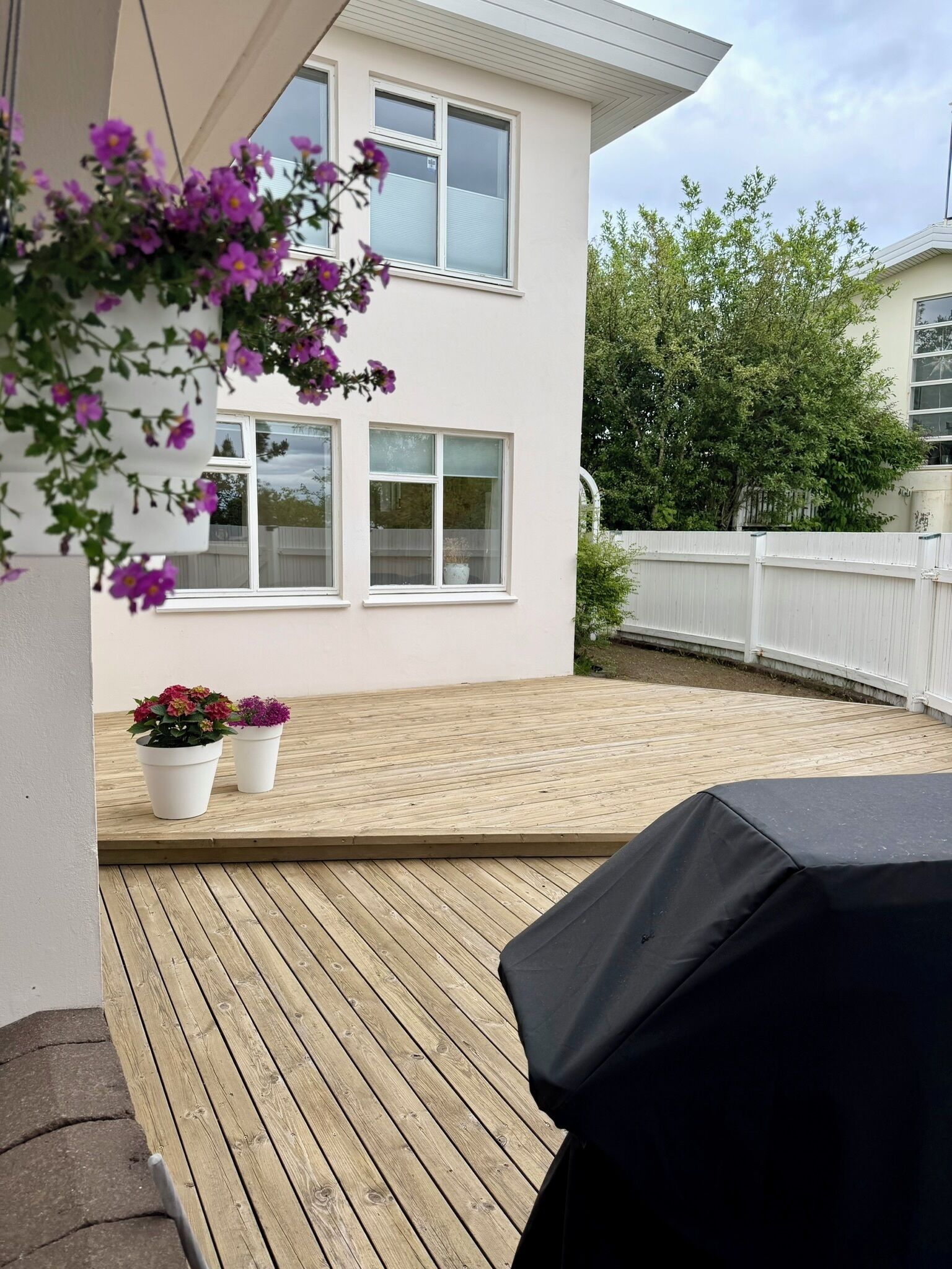A wooden deck with a covered grill area, white walls, and a white fence.