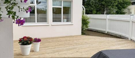 A wooden deck with a covered grill area, white walls, and a white fence.