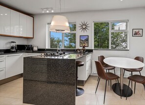 Een moderne keuken met een centraal eiland, een eetgedeelte met een ronde tafel en stoelen, en grote ramen met uitzicht op groen.