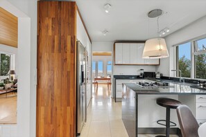 Een moderne keuken met een houten accentmuur, een groot eiland met barstoelen, en uitzicht op het buiten.