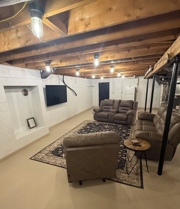 A basement with a fireplace, sofas, and a rug.