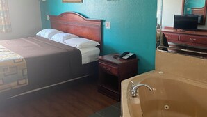 Habitación de hotel con cama, mesita de noche, teléfono, televisión, espejo y bañera.