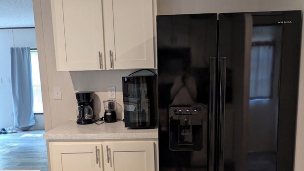 A compact kitchen with white cabinets, a black refrigerator, a coffee maker, and a water dispenser.