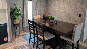 A dining area with a wooden table, four chairs, a potted plant, and a window with curtains.