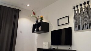 Ein moderner Essbereich mit einem Glastisch, schwarzen Stühlen, einer schwarzen Kommode, einem Flachbildfernseher und einem Wandbild.
