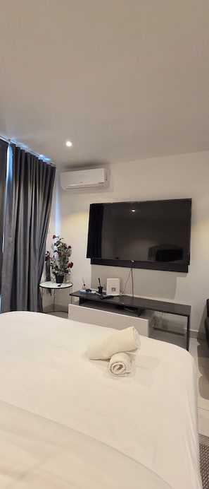 A hotel room with a bed, a flat-screen TV mounted on the wall, a small table with a potted plant, and an air conditioning unit. - ebs properties 2 two bedroom duplex (Accra)