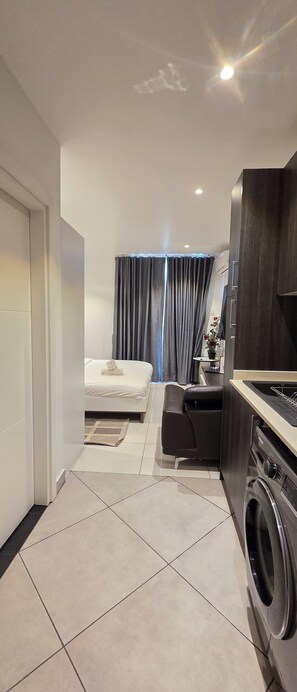 A modern hotel room with a bed, a small seating area, a washing machine, and a view of the outdoors. - ebs properties 2 two bedroom duplex (Accra)