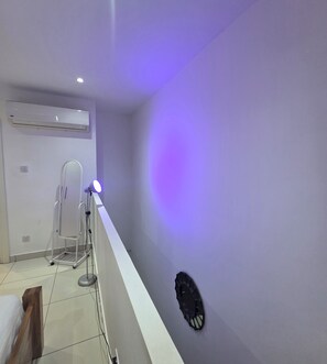 A hallway with a white ceiling, a wall-mounted air conditioning unit, and a floor lamp with a blue light. - ebs properties 2 two bedroom duplex (Accra)
