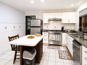 Eine moderne Küche mit weißen Schränken, Edelstahlgeräten und einem Essbereich mit Holztisch und Stühlen.