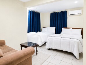 Een hotelkamer met twee bedden, een bank, een bijzettafeltje en een airconditioning.
