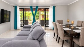 Ein Wohnzimmer mit grauem Sofa, einem Esstisch mit Stühlen und einem an der Wand befestigten Fernseher.