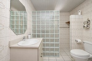 Een badkamer met een wit wastafelmeubel, een toilet en een douchegedeelte met geëtste glazen panelen.