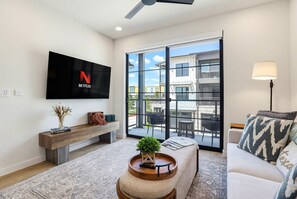 A modern living room with a flat-screen TV, a bench, a coffee table with a plant, and a sofa with patterned cushions. - Unwind in Style: Luxe Condo Getaway! (New Braunfels)