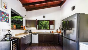 A modern kitchen with dark wood cabinets, stainless steel appliances, and a window with a view of greenery. - Beachfront Villa - Private Paradise (Le Robert)