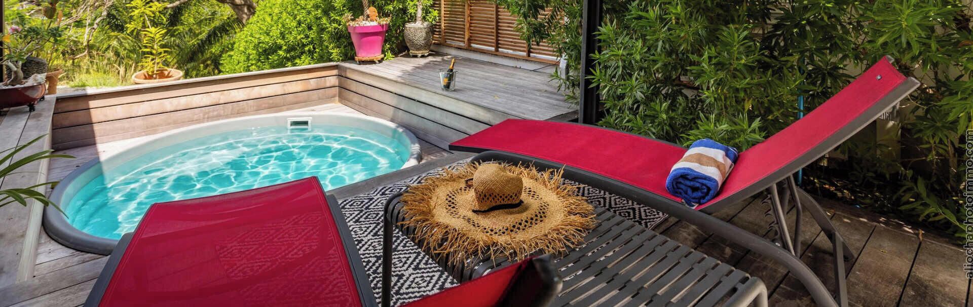 A hot tub with lounge chairs and a patterned mat, surrounded by greenery.