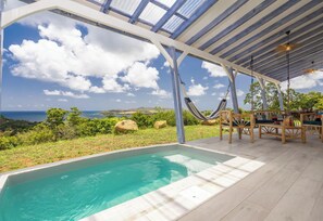 An outdoor pool area with a view of the ocean, wooden furniture, and a covered seating area. - Les Villas de Solange - Azur & Canopée (La Trinité)