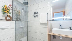 Een moderne badkamer met een douchecabine van glas, een witte wastafel en een spiegel.
